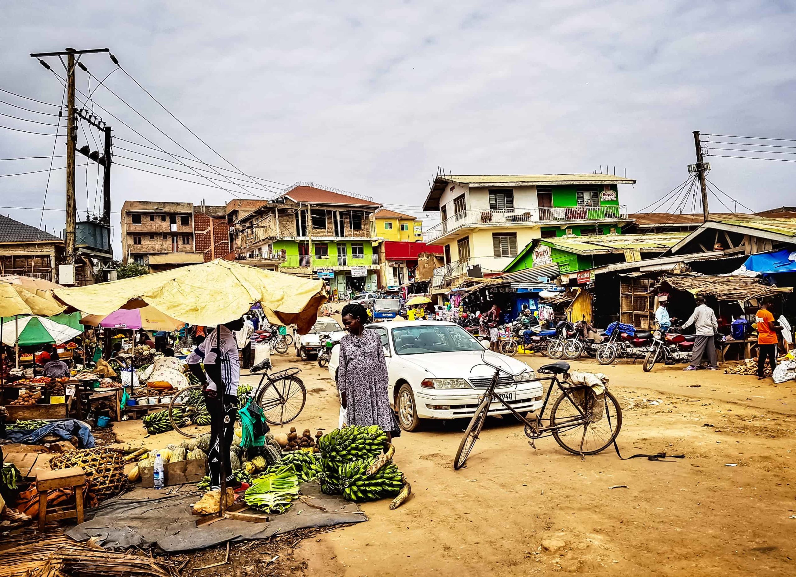 A suburban dirt road lined with fruit vendors and with a parked a car and bicycle