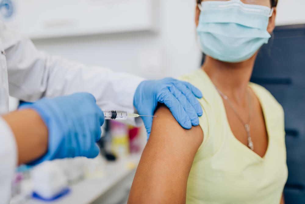 A close-up of a woman's shoulder as a medical professional administers a vaccine.