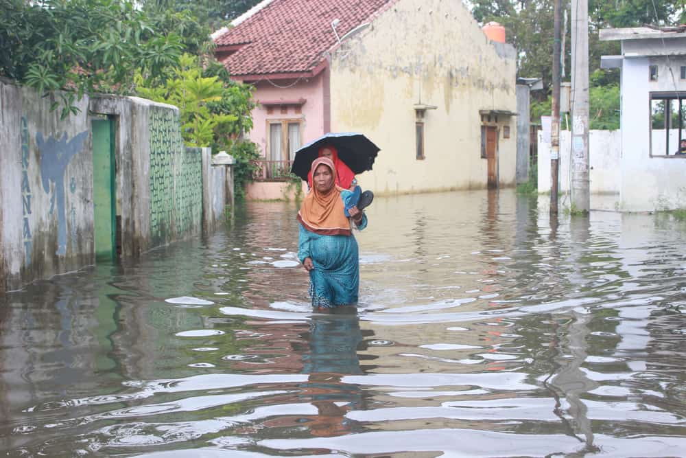 Woman walking through flood water in Indonesia, carrying a child on her back