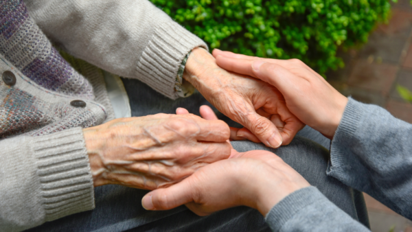 A pair of hands from an older person holding the hands of a younger person.