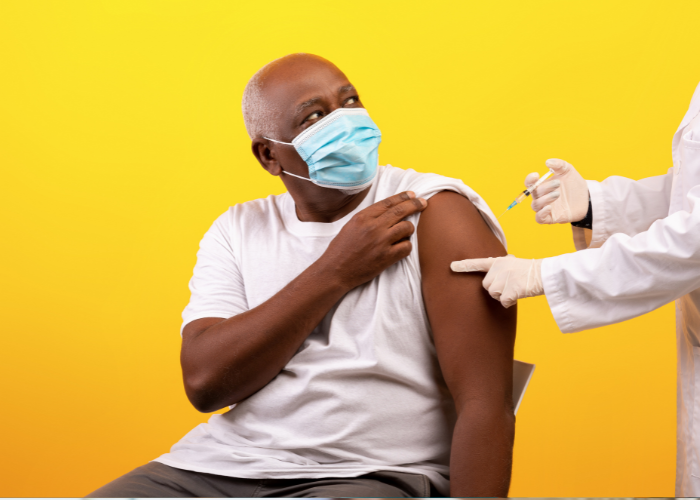 Older man in mask receiving a vaccine from a person mostly out of frame.