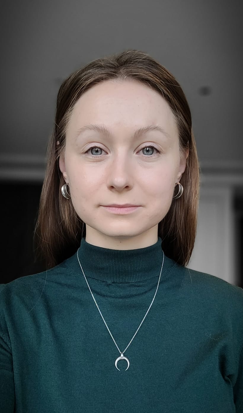 Women with brown hear, earings, a green turtle neck shirt, and a necklace over a neutral indoor background