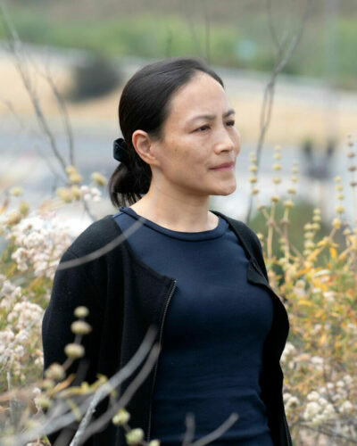 Jun Wu in a black blouse in a field of wild grass and flowers