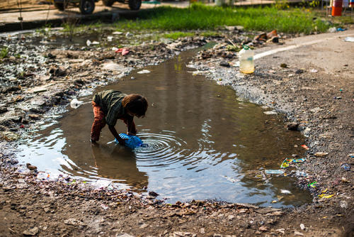 Child retrieving water from a puddle in an urban informal settlement