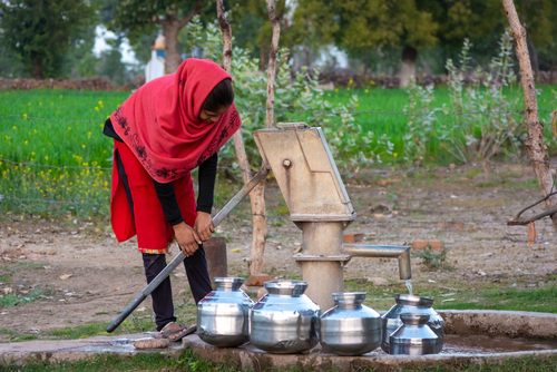 Woman in India using a hand pump to pull up ground water